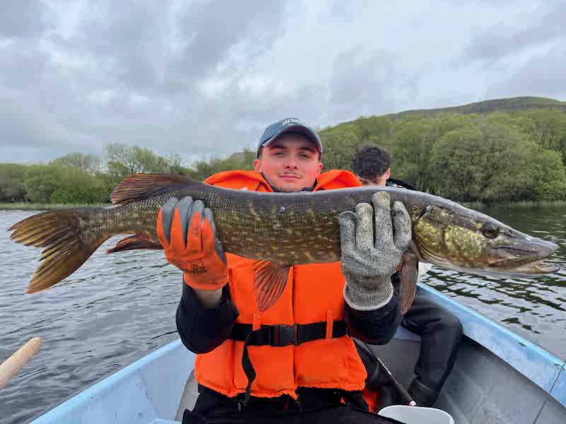 Pêcheur en gilet de sauvetage présentant un brochet en barque