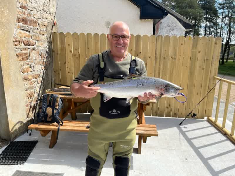 Pêcheur en waders présentant un saumon devant le cottage